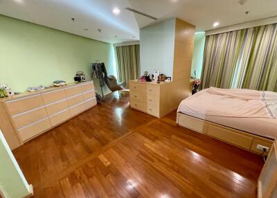 Spacious bedroom with wooden flooring, a bed, dresser, and a window with curtains