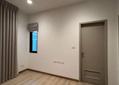 Empty bedroom with light wooden flooring, a small window with curtains, and a closed door