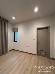 Empty bedroom with light wooden flooring, a small window with curtains, and a closed door