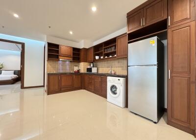 Modern kitchen with wooden cabinets, stainless steel refrigerator, washing machine, and appliances