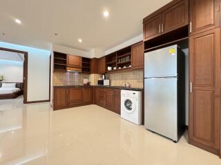 Modern kitchen with wooden cabinets, stainless steel refrigerator, washing machine, and appliances