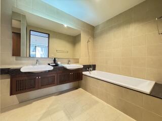 Modern bathroom with large mirror, dual sinks, and bathtub.