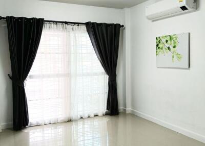 Bright living room with large window, black curtains, and air conditioning unit