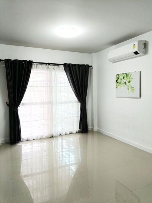 Bright living room with large window, black curtains, and air conditioning unit