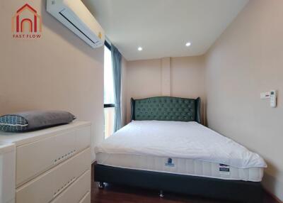 A modern bedroom with an elegant green headboard, white dresser, air conditioning, and natural light.