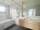 Modern bathroom with bathtub, glass shower partition, dual sinks, and large mirror