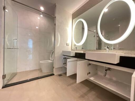 Modern bathroom with glass shower, double sink vanity with round mirrors, and open cabinets