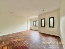 Spacious living room with wooden parquet flooring and multiple windows