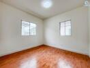 Empty bedroom with wooden floor and two windows