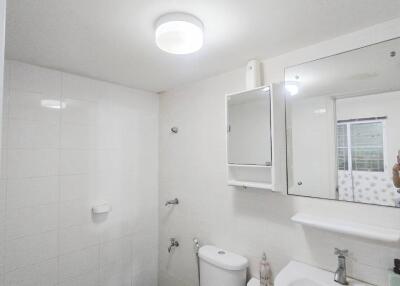 Modern bathroom with white tiles, toilet, sink, and mirrored cabinet