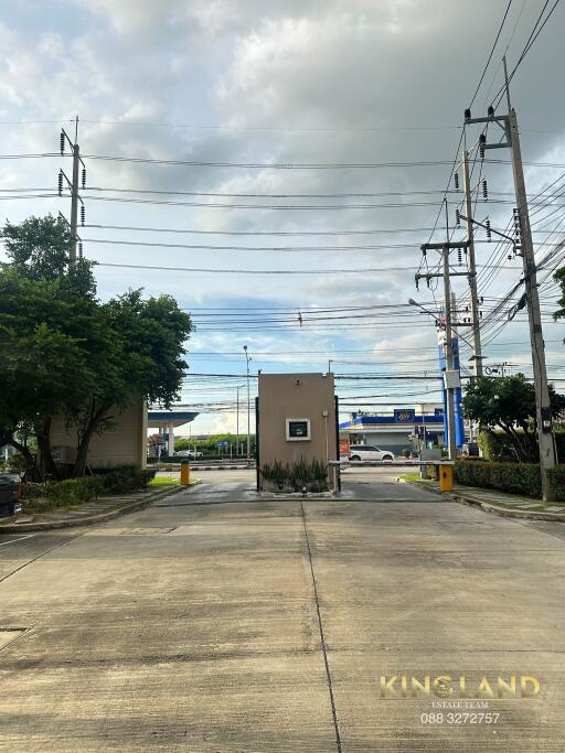 Photo of the entrance to a residential complex with surrounding greenery and power lines.