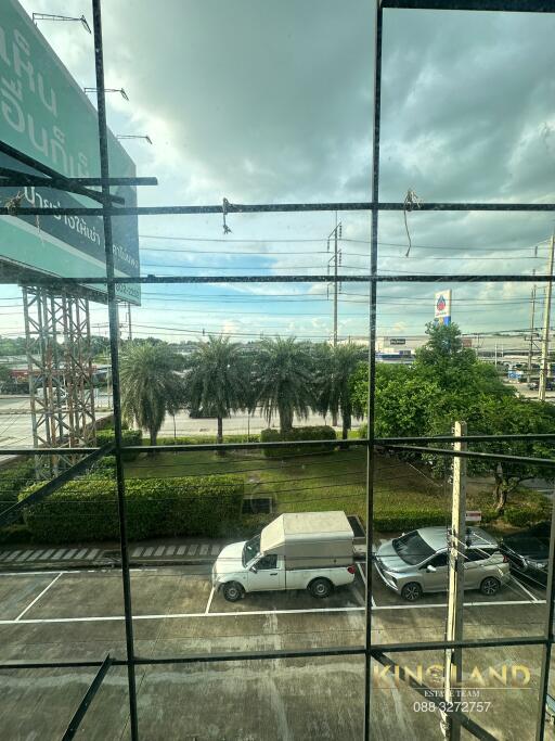 View from the window showing a parking lot, road, and palm trees with a cloudy sky.