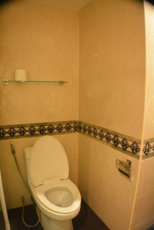 Small bathroom with toilet, decorative tile trim, and wall-mounted toilet roll holder