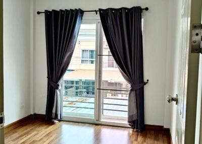 A bedroom with wooden flooring, large window, and dark curtains