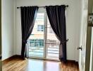 A bedroom with wooden flooring, large window, and dark curtains