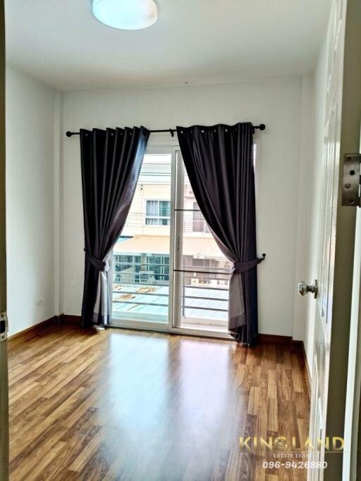 A bedroom with wooden flooring, large window, and dark curtains