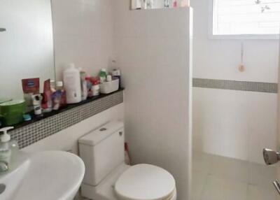 A well-lit bathroom with essential amenities including a sink, toilet, mirror, and storage shelf.