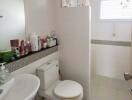 A well-lit bathroom with essential amenities including a sink, toilet, mirror, and storage shelf.