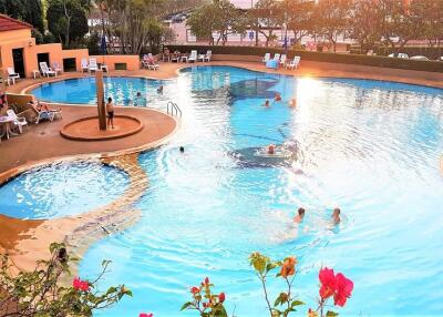 Spacious swimming pool area with lounge chairs and people swimming