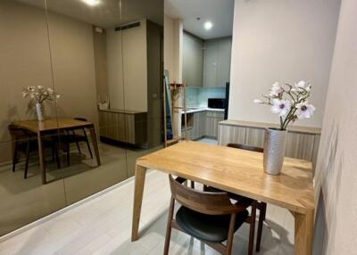 Dining area with wooden table and chairs, mirrored wall, and view into the kitchen