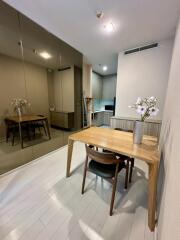 Dining area with wooden table and chairs, mirrored wall, and view into the kitchen