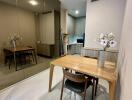 Dining area with wooden table and chairs, mirrored wall, and view into the kitchen