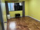 Bright empty bedroom with wooden floors, a window, an air conditioner, and a small table