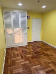 A brightly lit room with wooden parquet flooring, yellow walls, a white door, and a white wardrobe with louvered doors.