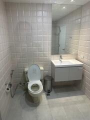 A bathroom with a toilet, sink, mirror, and tiled walls