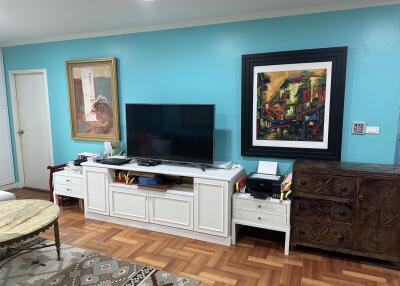 Living room with wooden flooring and blue walls featuring a television, decorative art, and furniture