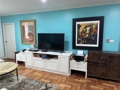 Living room with wooden flooring and blue walls featuring a television, decorative art, and furniture