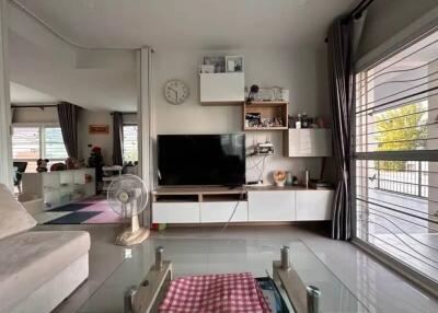 Modern living room with a TV, glass coffee table, and large windows