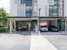 Modern residential building with two cars parked in the driveway and an outdoor seating area