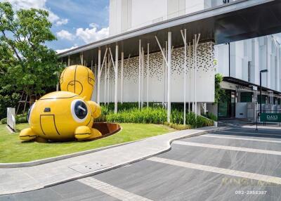 Modern building entrance with a unique yellow sculpture and green landscaping