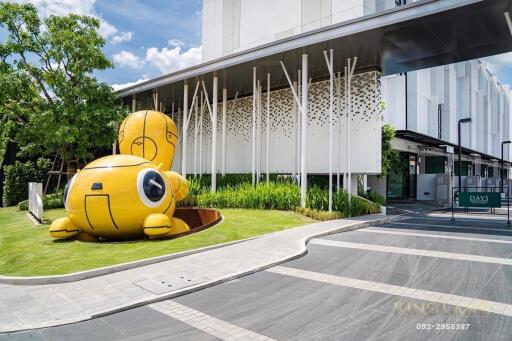 Modern building entrance with a unique yellow sculpture and green landscaping