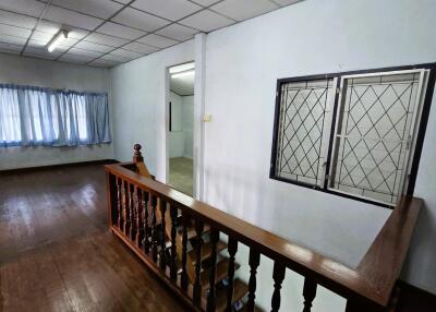 Spacious bedroom with wooden floor, window with bars, and curtains