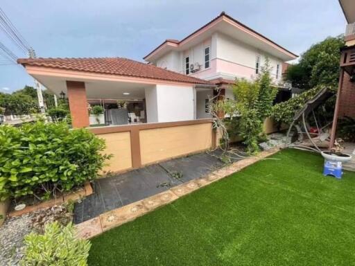 Front yard of a house with green artificial grass, a swing set, and a two-story house