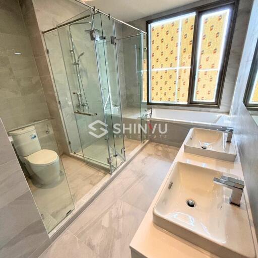 Modern bathroom with glass shower, toilet, and double sink