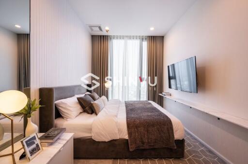 Modern bedroom with a large bed, mounted TV, and a window with curtains