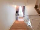 Interior view of a staircase with wooden steps and a railing, leading to a room with curtains and natural light