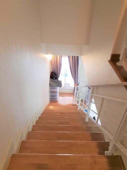 Interior view of a staircase with wooden steps and a railing, leading to a room with curtains and natural light