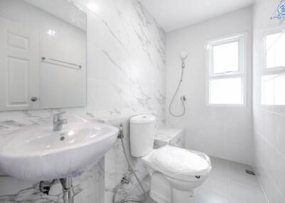 Clean modern bathroom with white marble walls, a toilet, sink, mirror, and shower