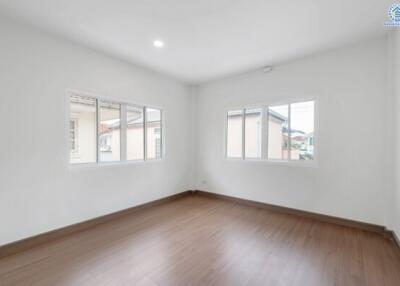 Empty bedroom with wooden flooring and large windows.