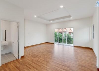 Spacious, well-lit living room with wooden flooring and large window doors leading to a balcony.