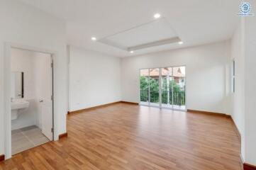 Spacious, well-lit living room with wooden flooring and large window doors leading to a balcony.