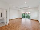 Spacious, well-lit living room with wooden flooring and large window doors leading to a balcony.