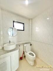 Modern bathroom with white tiles, a countertop basin, toilet, and window