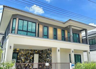 Modern two-story house with a stone facade, large windows, and gated driveway