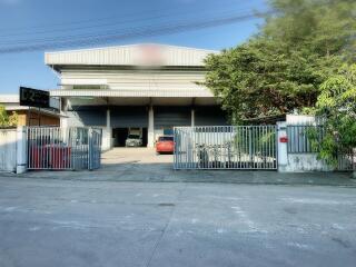 Industrial building with gated entrance, parking area, and surrounding greenery