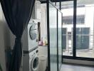 Laundry area with stacked washer and dryer, next to a large window